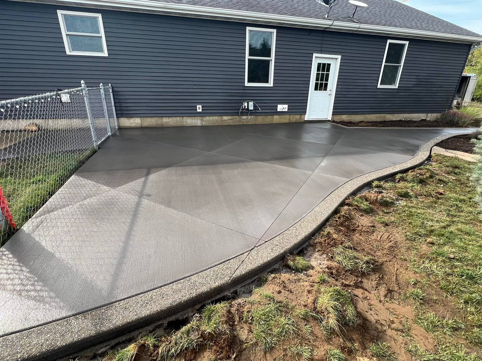 Colored concrete patio with exposed aggregate border behind a home