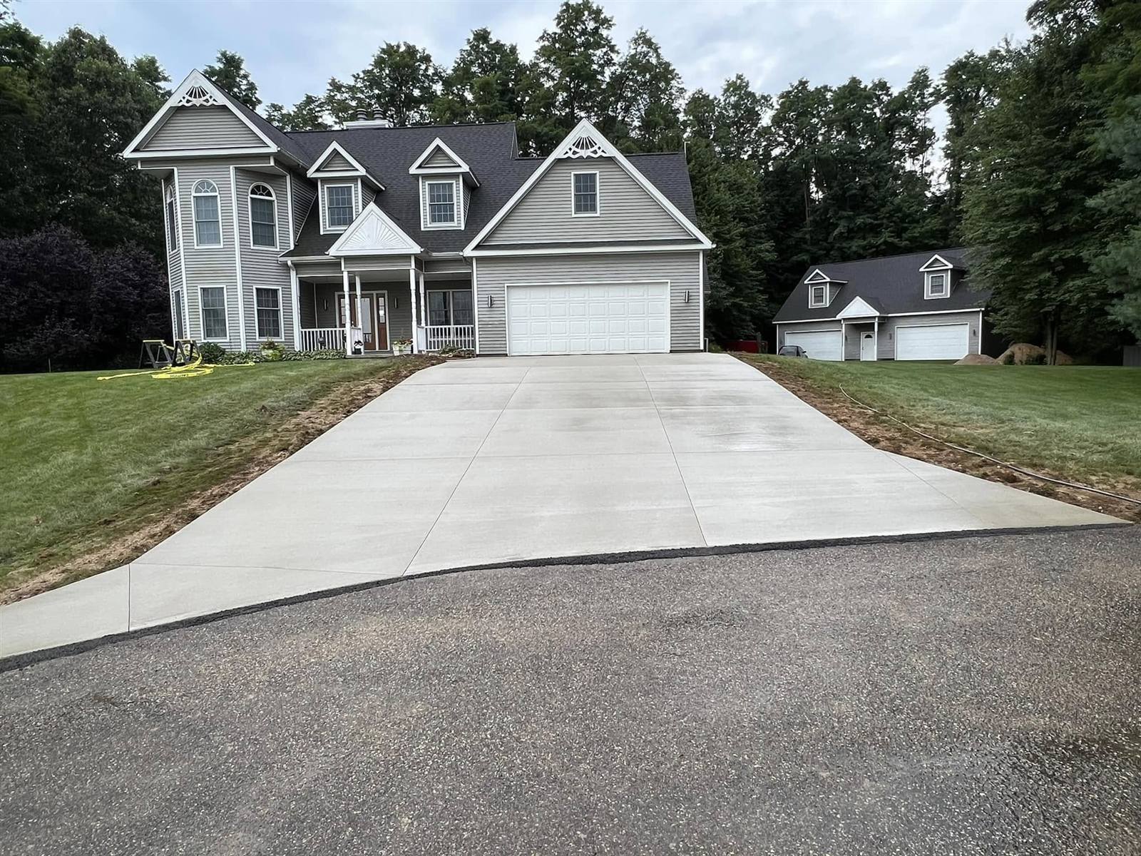 Wide concrete driveway with fresh grading in front of a large house